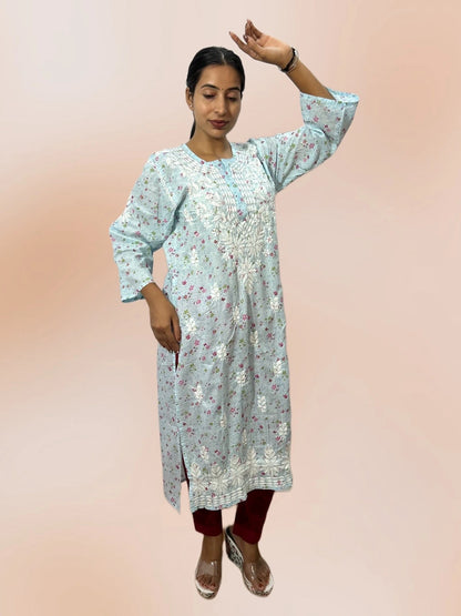 A woman modeling a light blue floral printed kurta with silver mirror work embroidery, paired with maroon pants and clear high-heeled sandals, set against a solid peach-pink studio background.