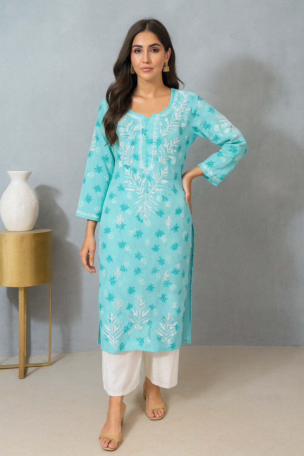 Woman wearing a light blue embroidered kurta with white pants against a gray background