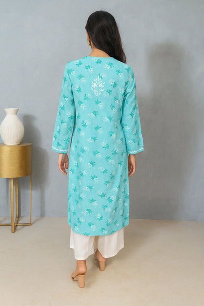 Woman wearing a turquoise embroidered kurta with white pants against a gray background