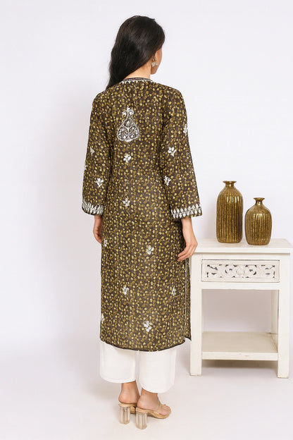 Lucknowi chikankari Woman wearing a green patterned kurta with white pants, standing in front of a white wall with decorative vases.
