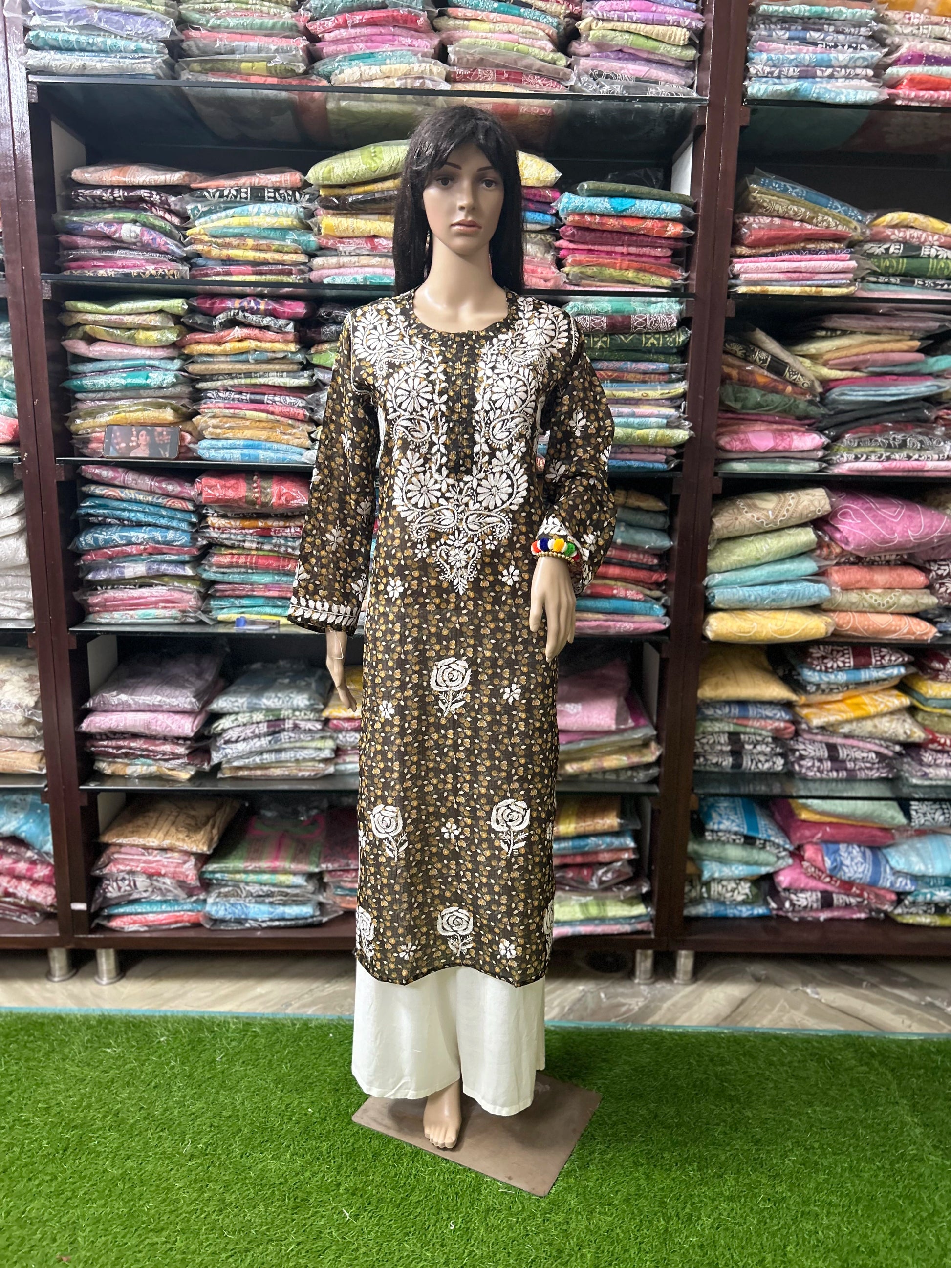 lucknowi chikankari Mannequin wearing a patterned dress in front of shelves filled with colorful fabric.
