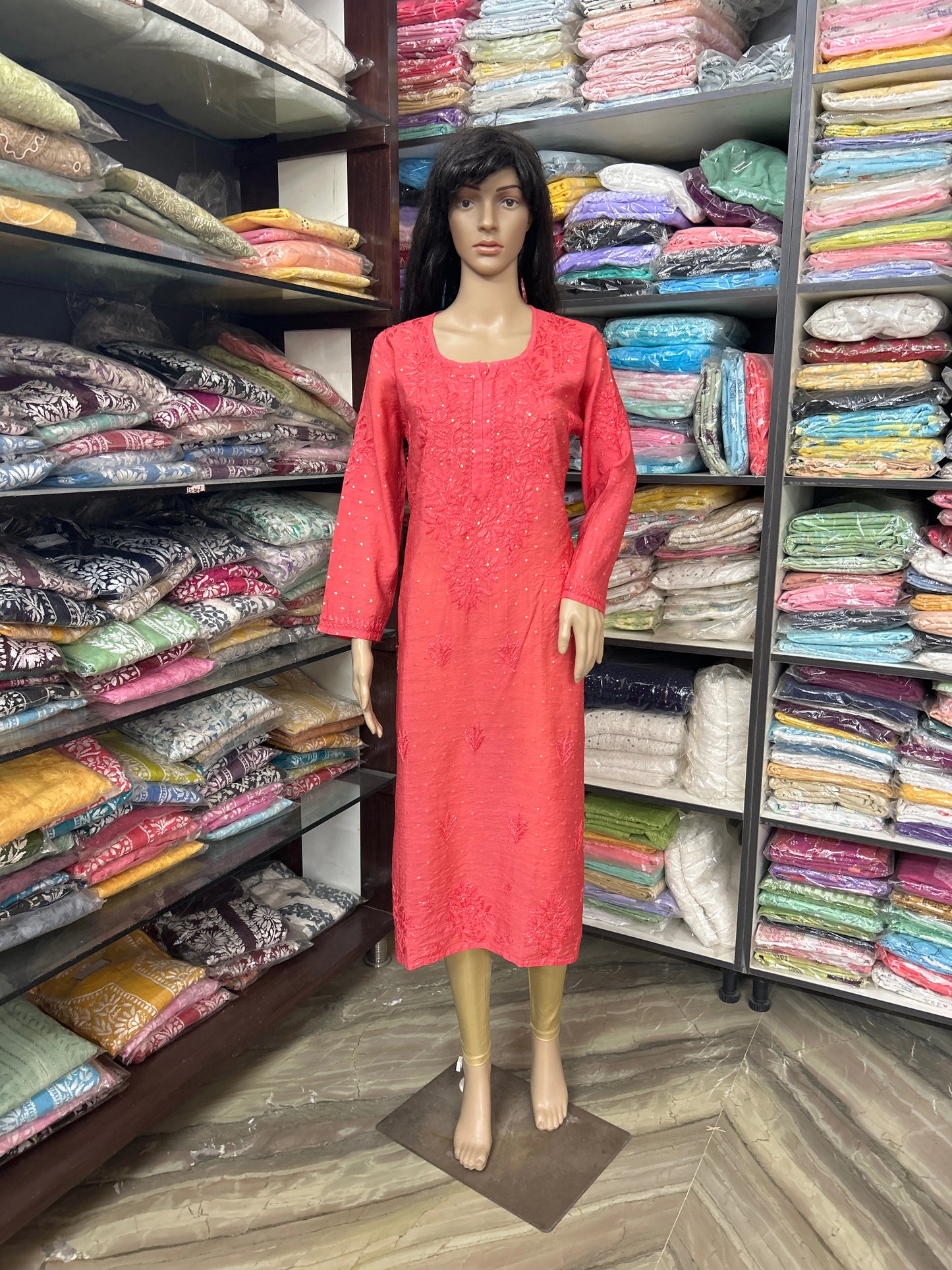 lucknowi chikankari Mannequin wearing a red dress in a fabric store with shelves of colorful fabrics.