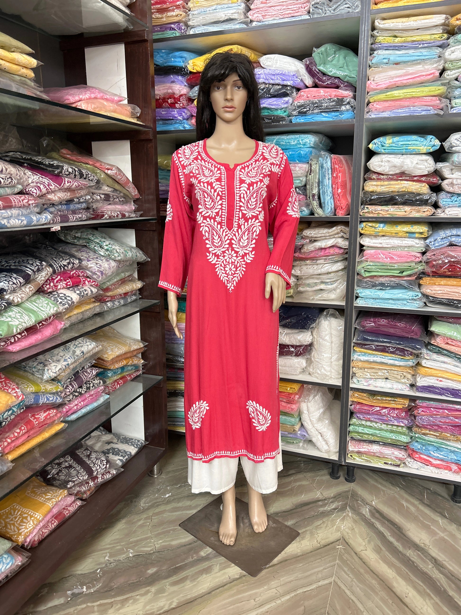 Mannequin wearing a red dress with white embroidery in a fabric store.