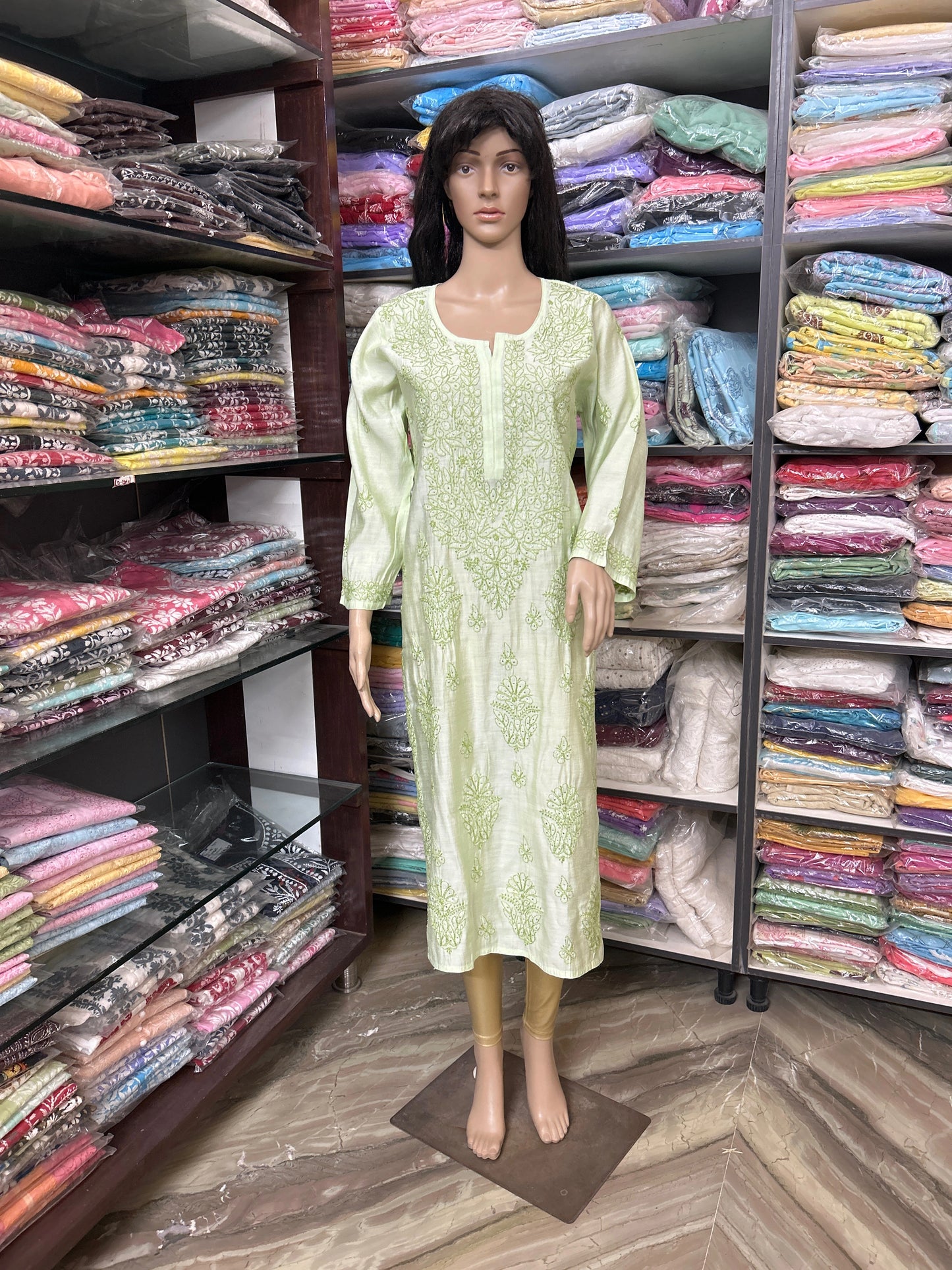Mannequin wearing a light green dress in a fabric store with shelves of colorful fabrics.