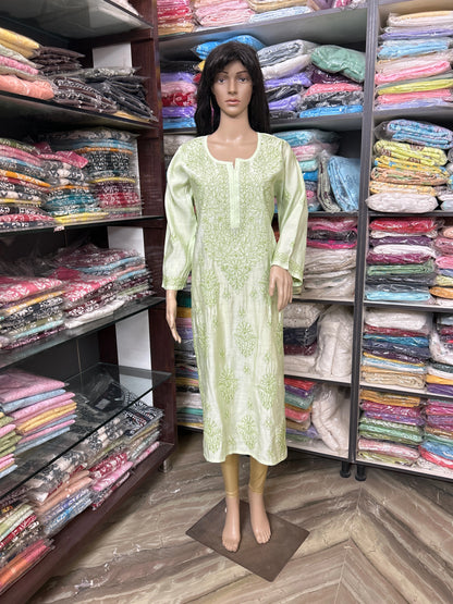 Mannequin wearing a light green dress in a fabric store with shelves of colorful fabrics.