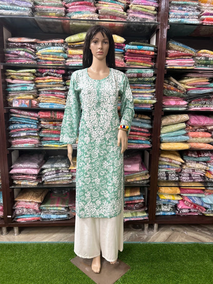 lucknowi chikankari Mannequin wearing a green and white traditional outfit in front of shelves filled with colorful fabrics.
