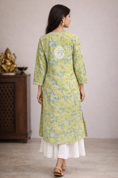 Woman wearing a lucknowi chikankari green floral kurta with white pants in a minimal indoor setting.