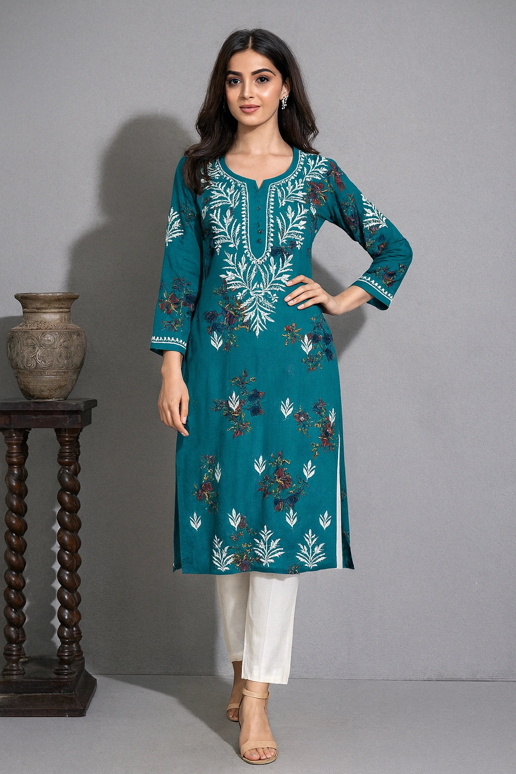 Woman wearing a teal embroidered kurta with white pants against a gray background