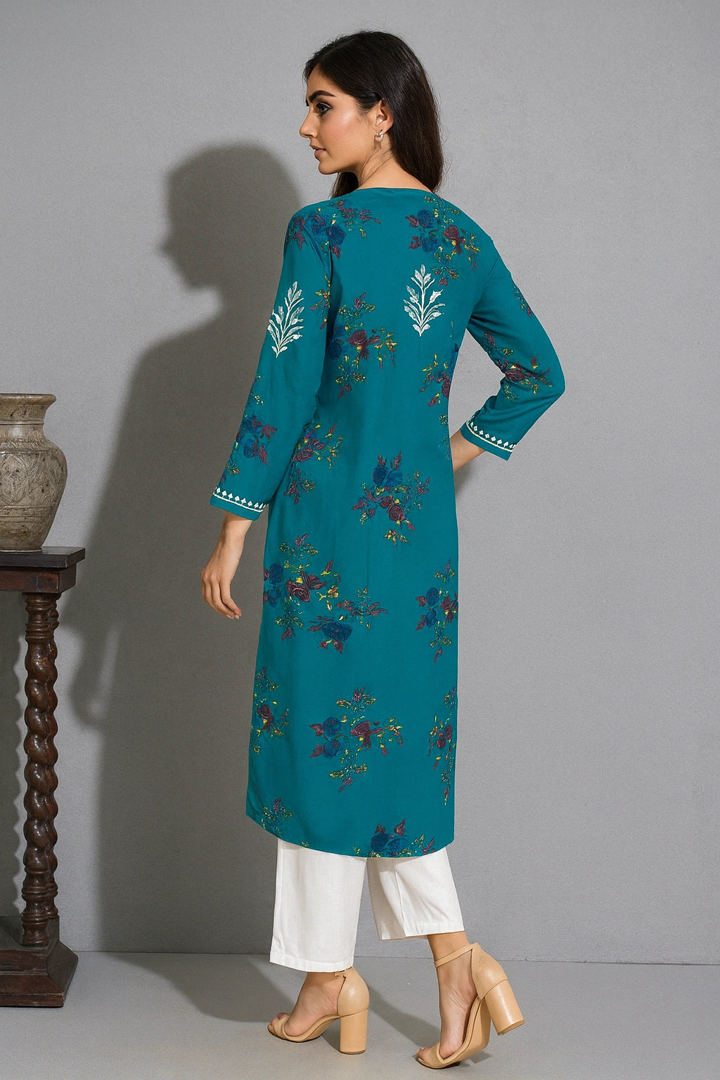 Woman wearing a teal embroidered kurta with white pants against a gray background