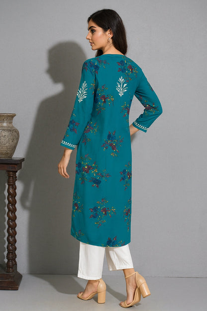 Woman wearing a teal embroidered kurta with white pants against a gray background