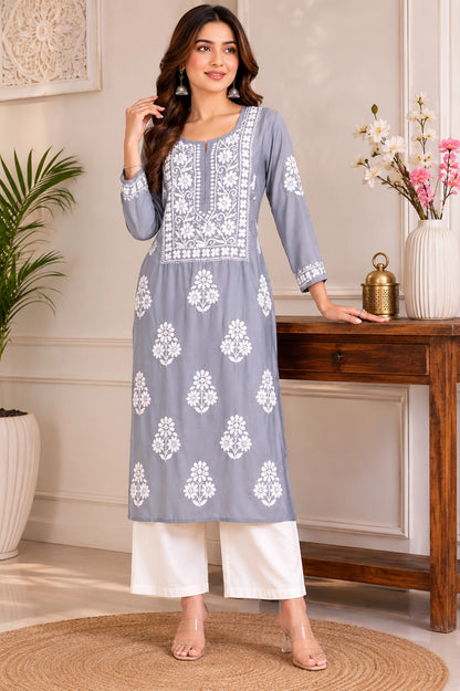 Woman wearing a gray kurta with white floral embroidery in a home setting.