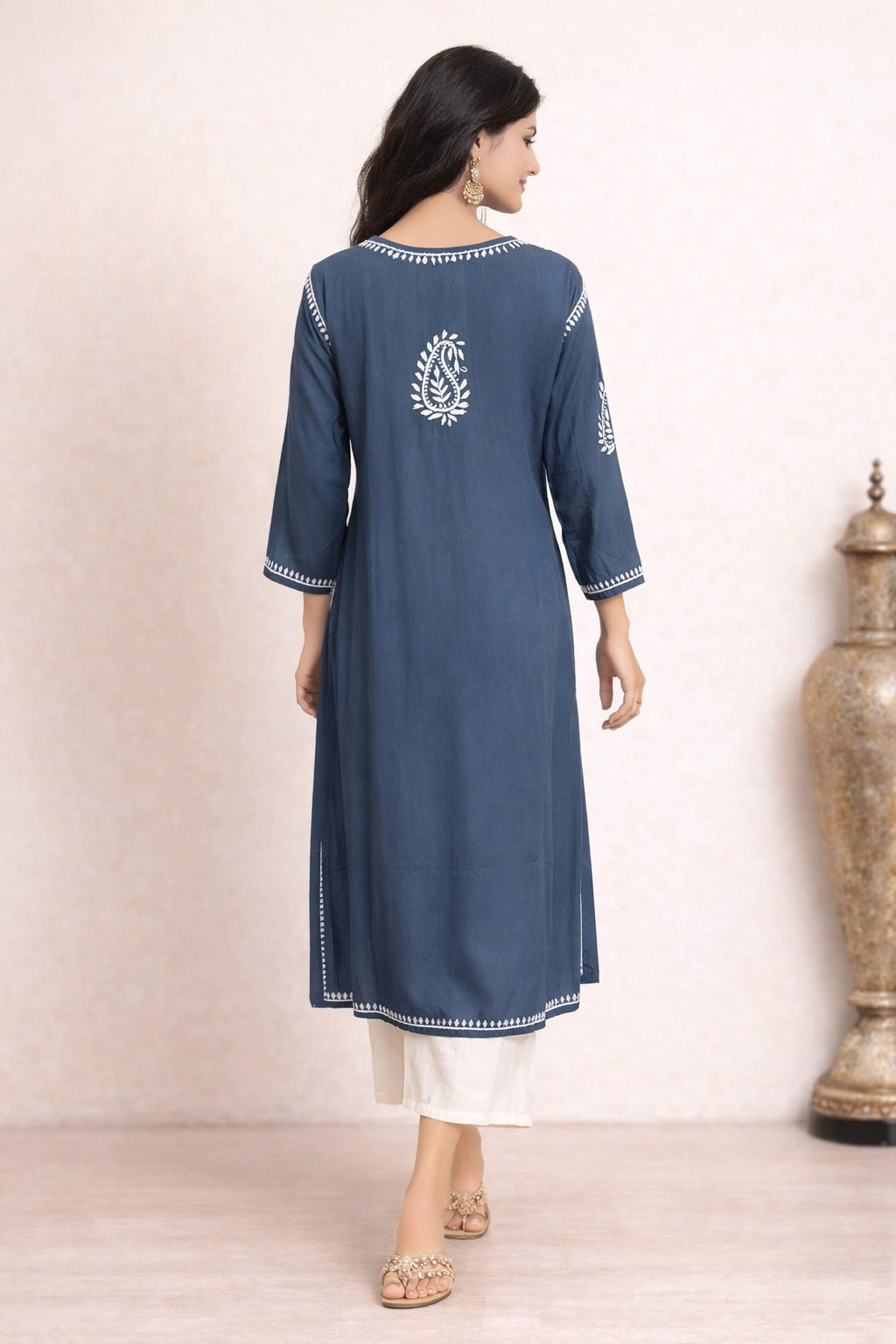 Woman wearing a blue embroidered kurta with white pants against a beige background