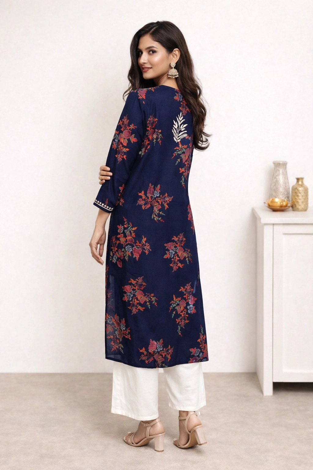Lucknowi chikankari A woman modeling a navy blue kurta with a red and orange floral print, paired with white pants and beige heels, shown from a back-three-quarter view in an indoor setting.