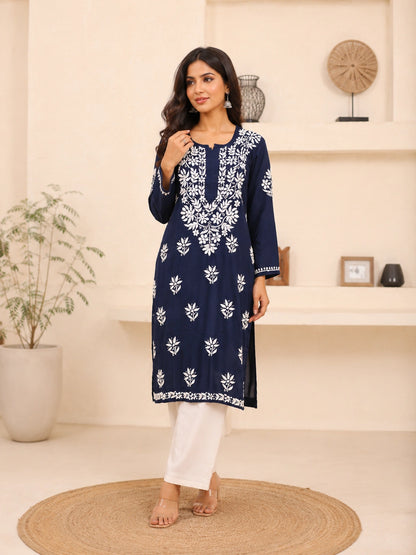 Woman wearing a blue embroidered kurta with white pants in an indoor setting.