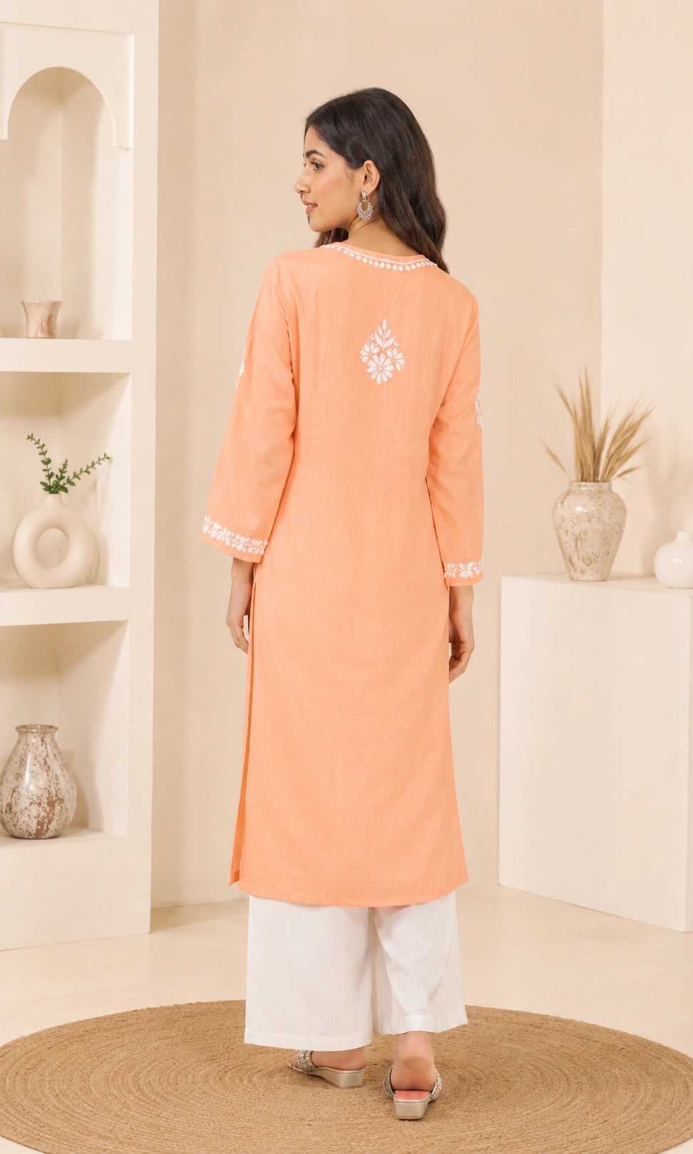Woman wearing a peach kurta with white embroidery in a minimalistic room.