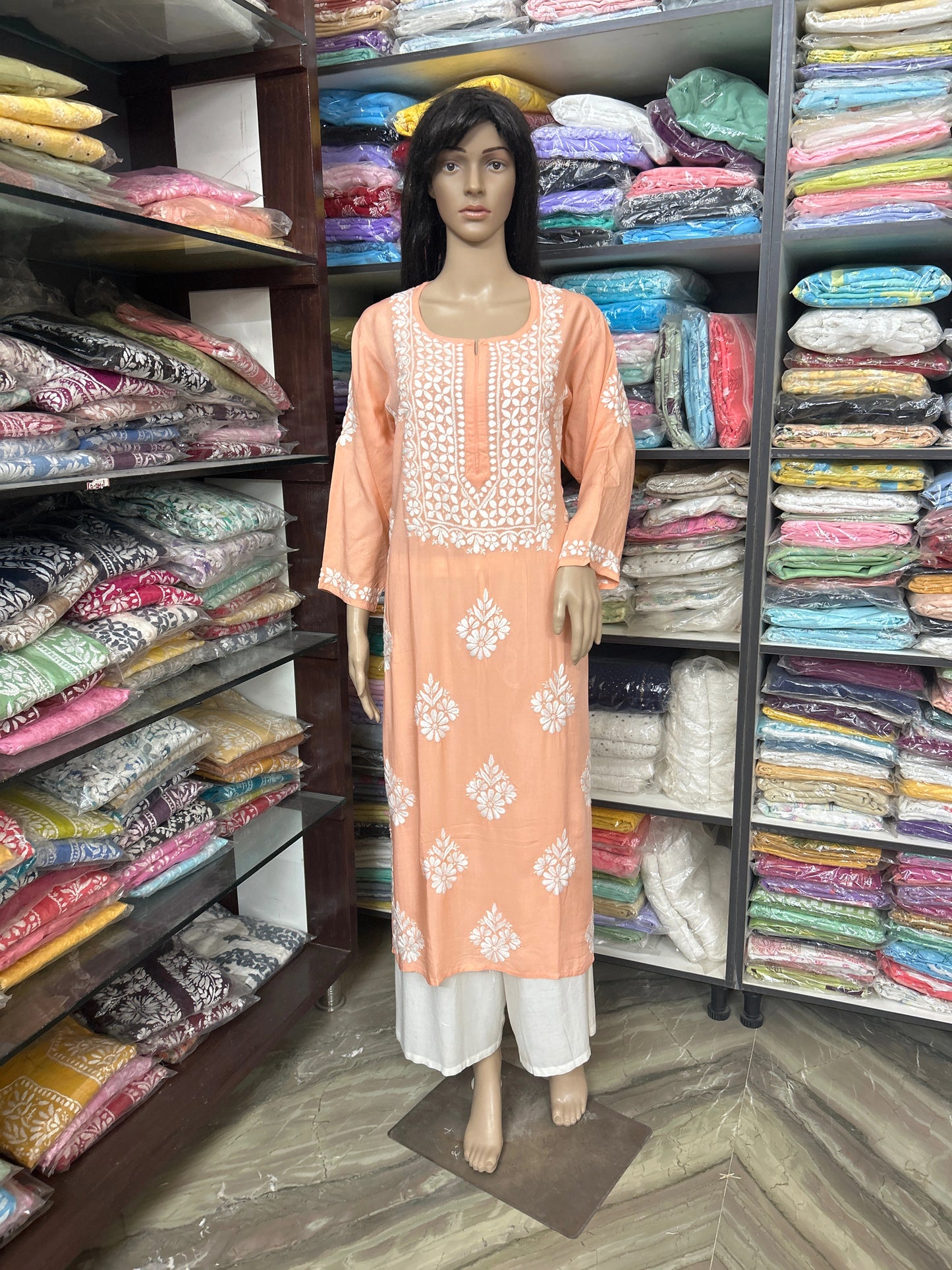 Mannequin wearing a peach embroidered kurta with a colorful fabric display in the background.