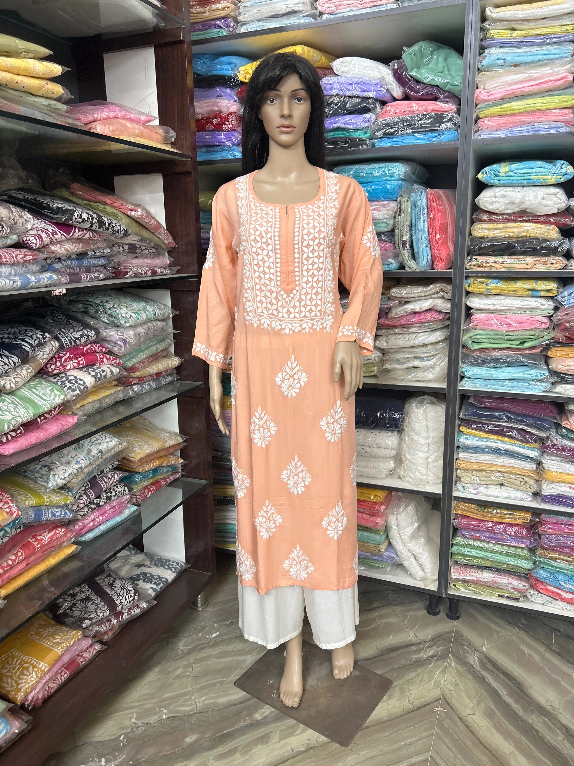 Mannequin wearing a peach embroidered kurta with a colorful fabric display in the background.