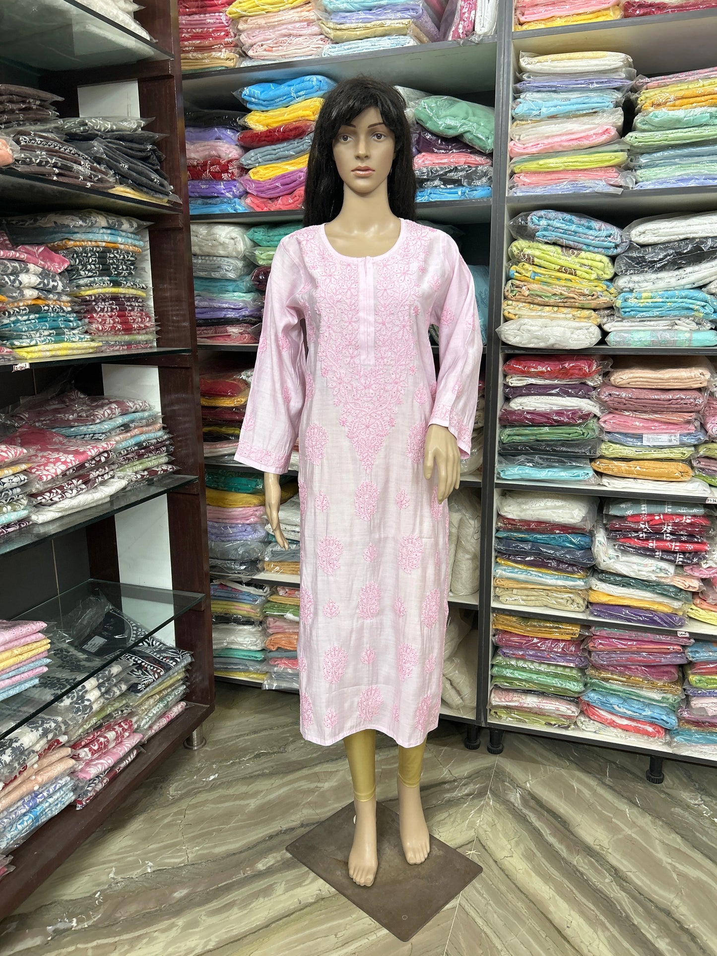 lucknowi chikankari Mannequin wearing a pink dress in a fabric store with shelves of colorful fabrics.