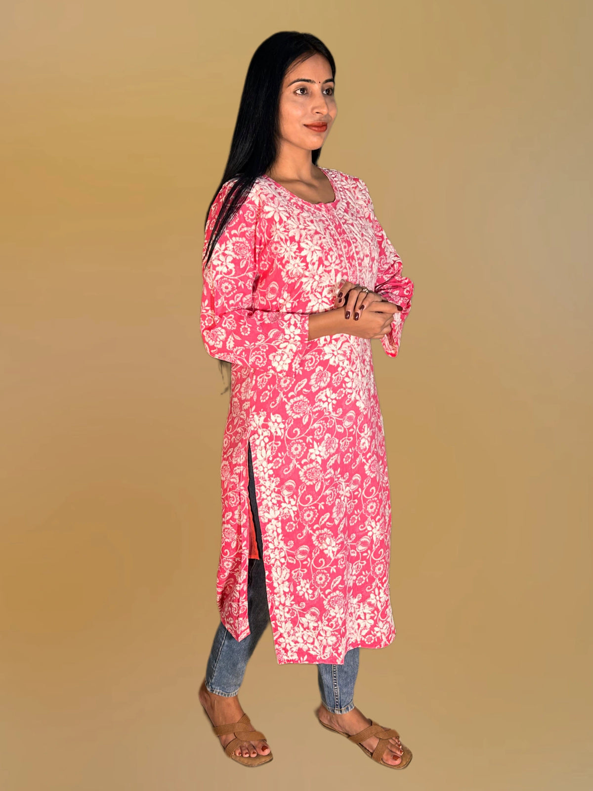 Lucknowi chikankari A woman modeling a pink and white floral print kurta with three-quarter sleeves, paired with blue jeans and brown sandals, set against a solid beige background.