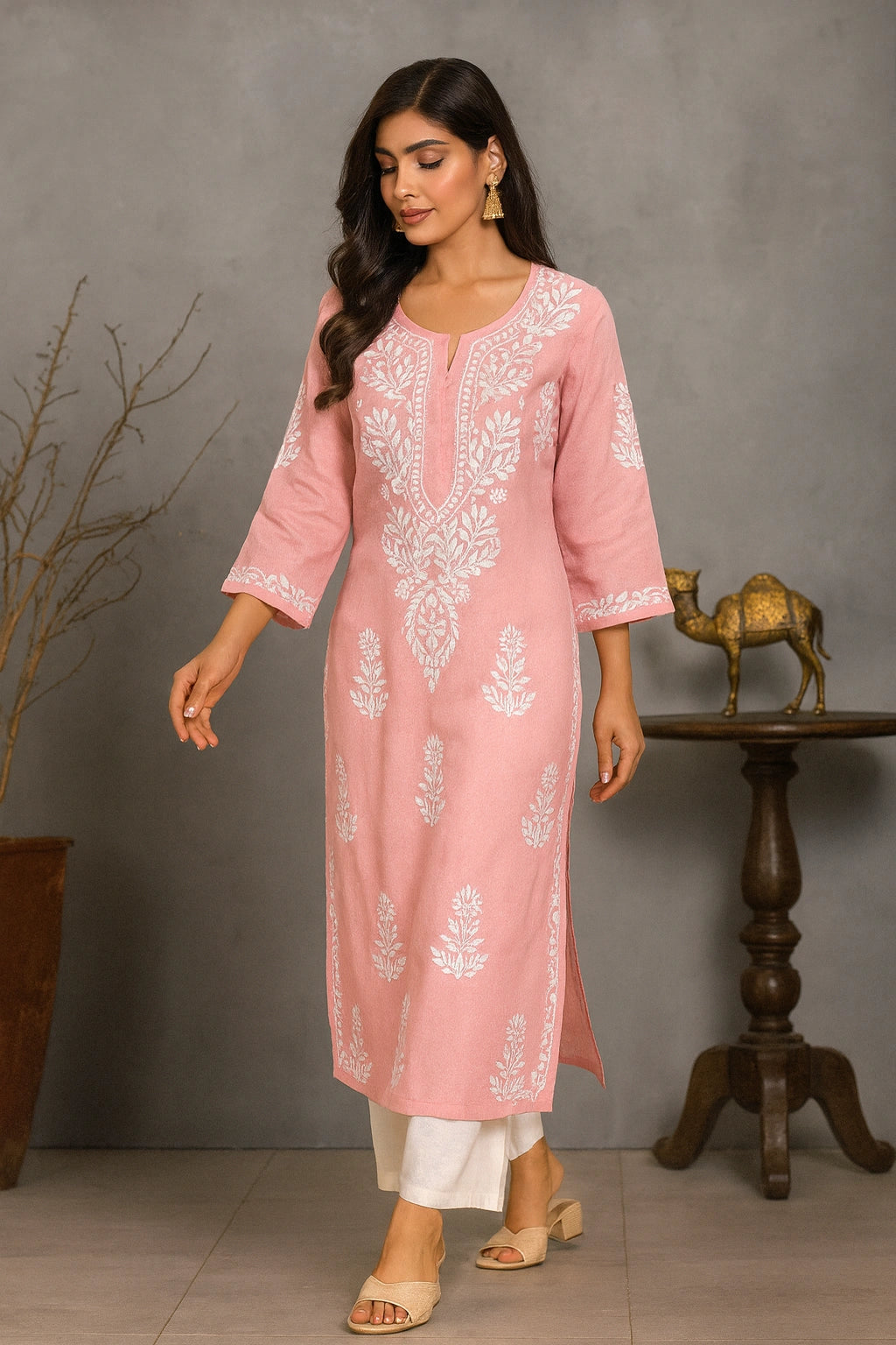 Woman wearing a pink embroidered kurta with white pants against a gray background