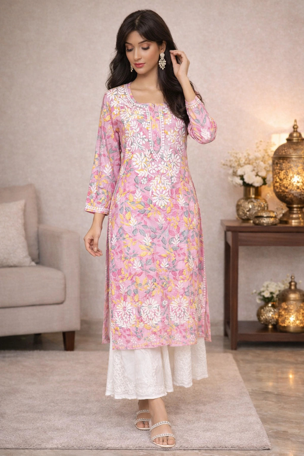 Woman wearing a lucknowi chikankari  floral pink and white kurta with white pants in a home setting.