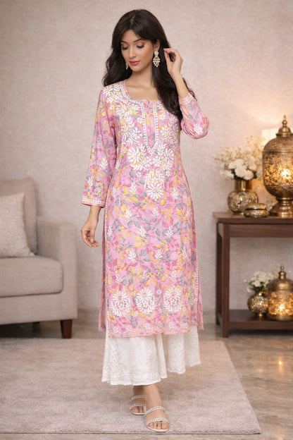 Woman wearing a lucknowi chikankari  floral pink and white kurta with white pants in a home setting.