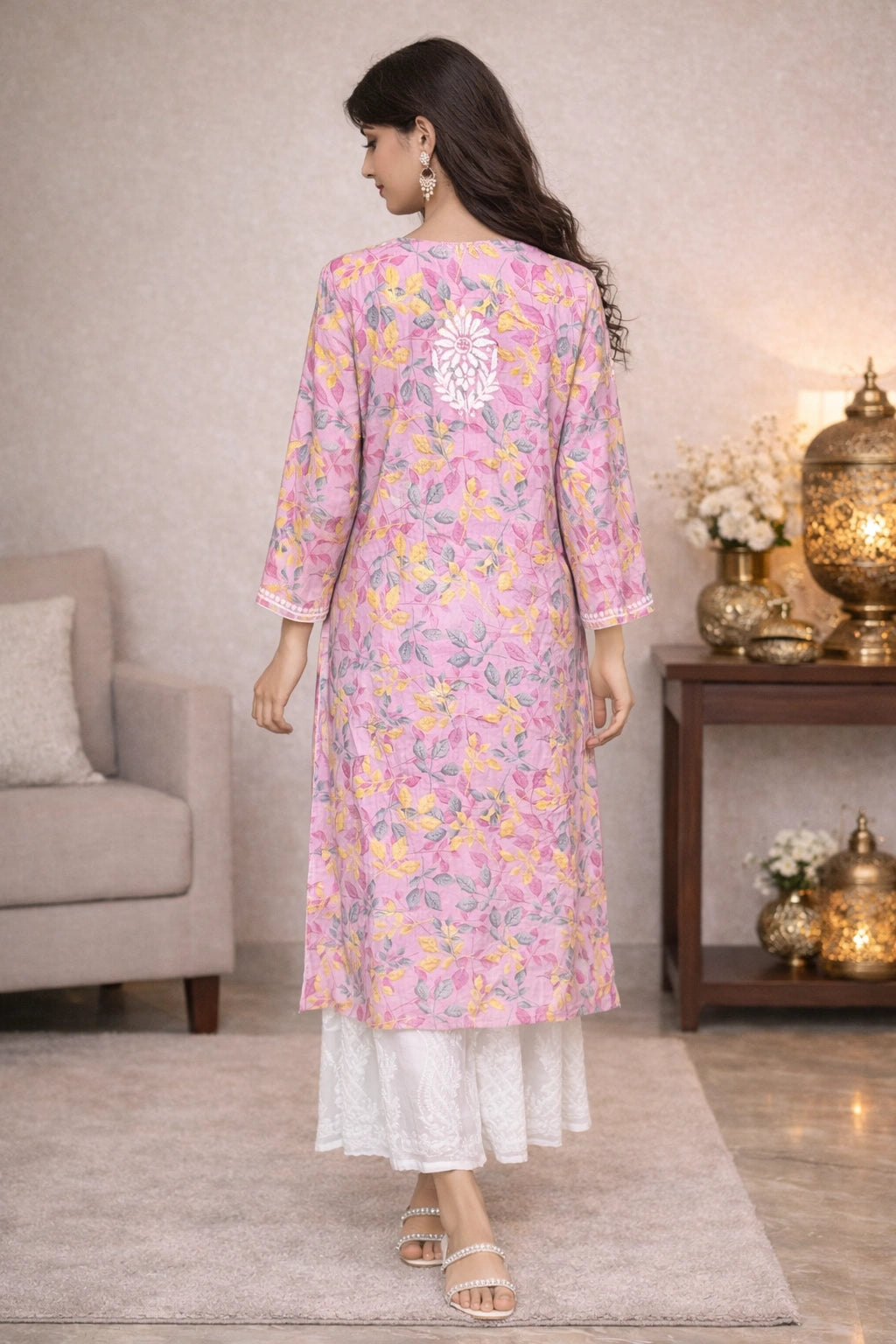 Woman wearing a lucknowi chikankari pink floral kurta with white pants in a living room setting.