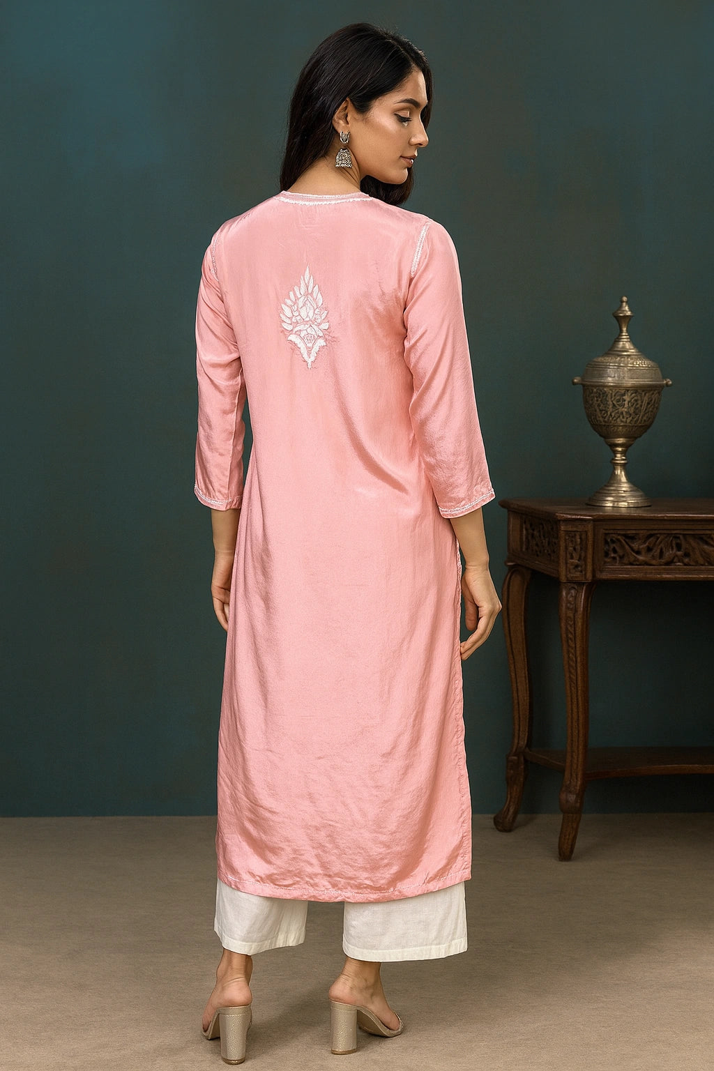 Woman wearing a pink kurta with white embroidery, standing against a dark green wall.