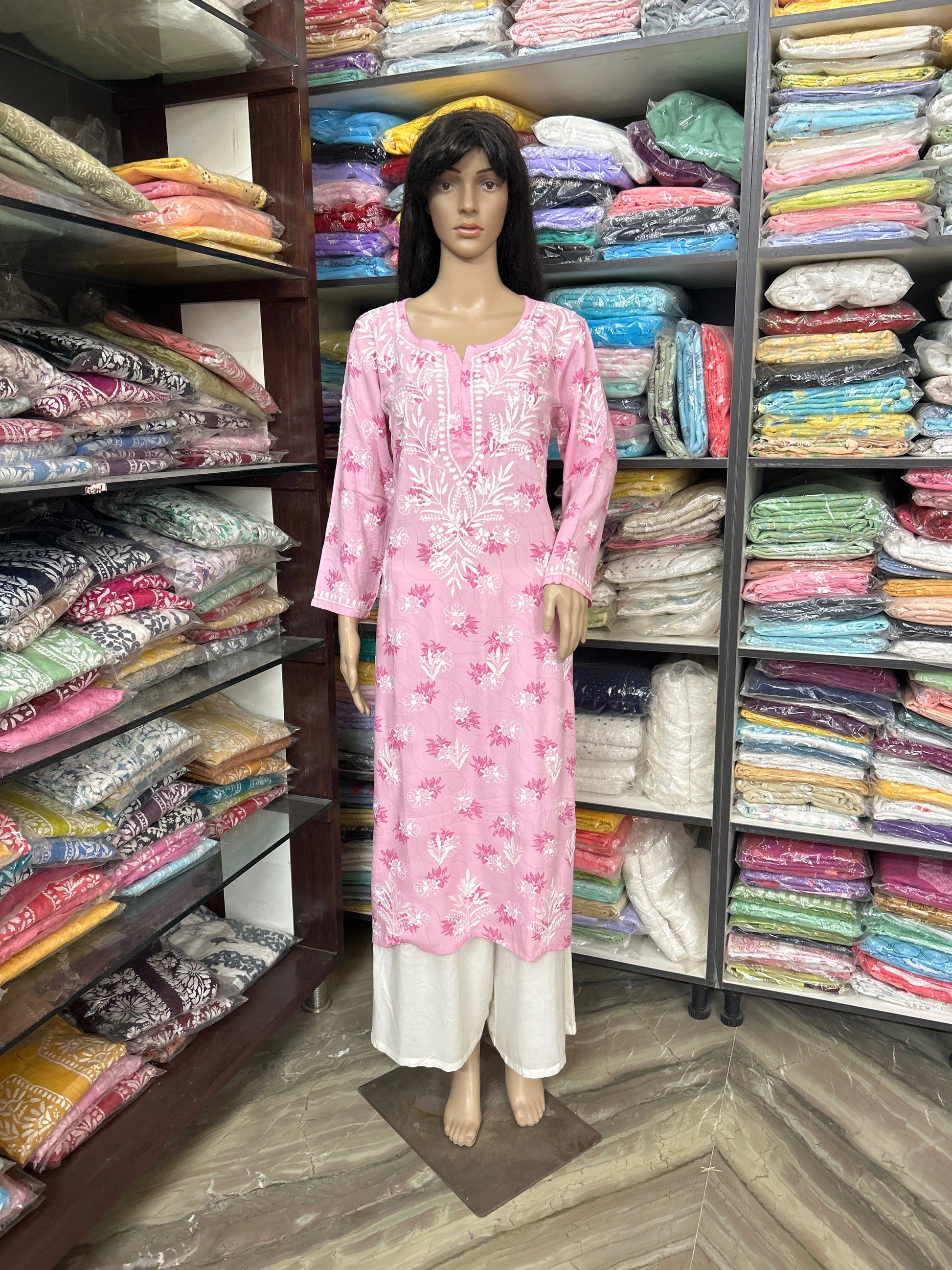 lucknowi chikankari Mannequin wearing a pink dress in a fabric store with shelves of colorful fabrics.