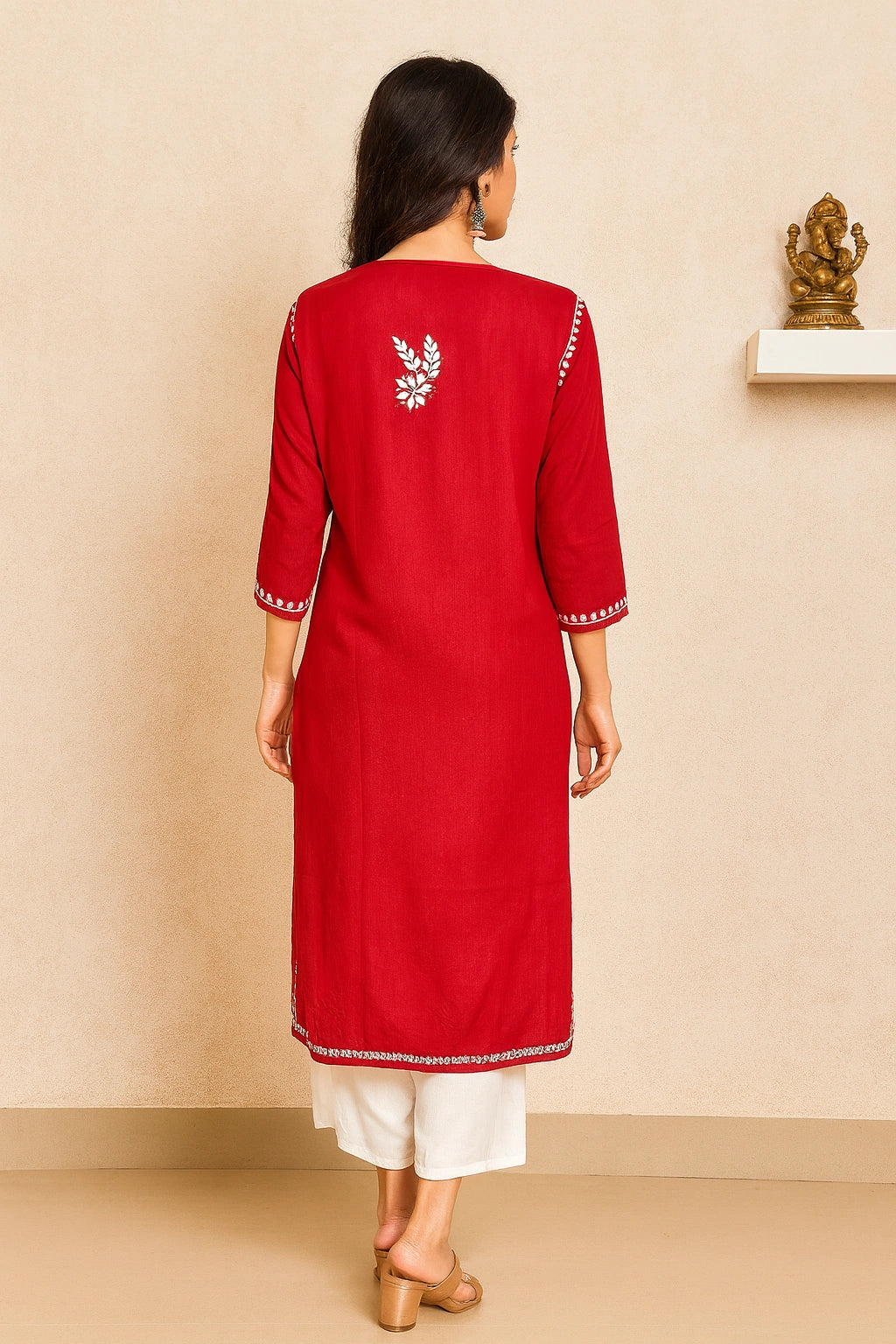 Woman wearing a red kurta with white embroidery, standing against a beige wall.