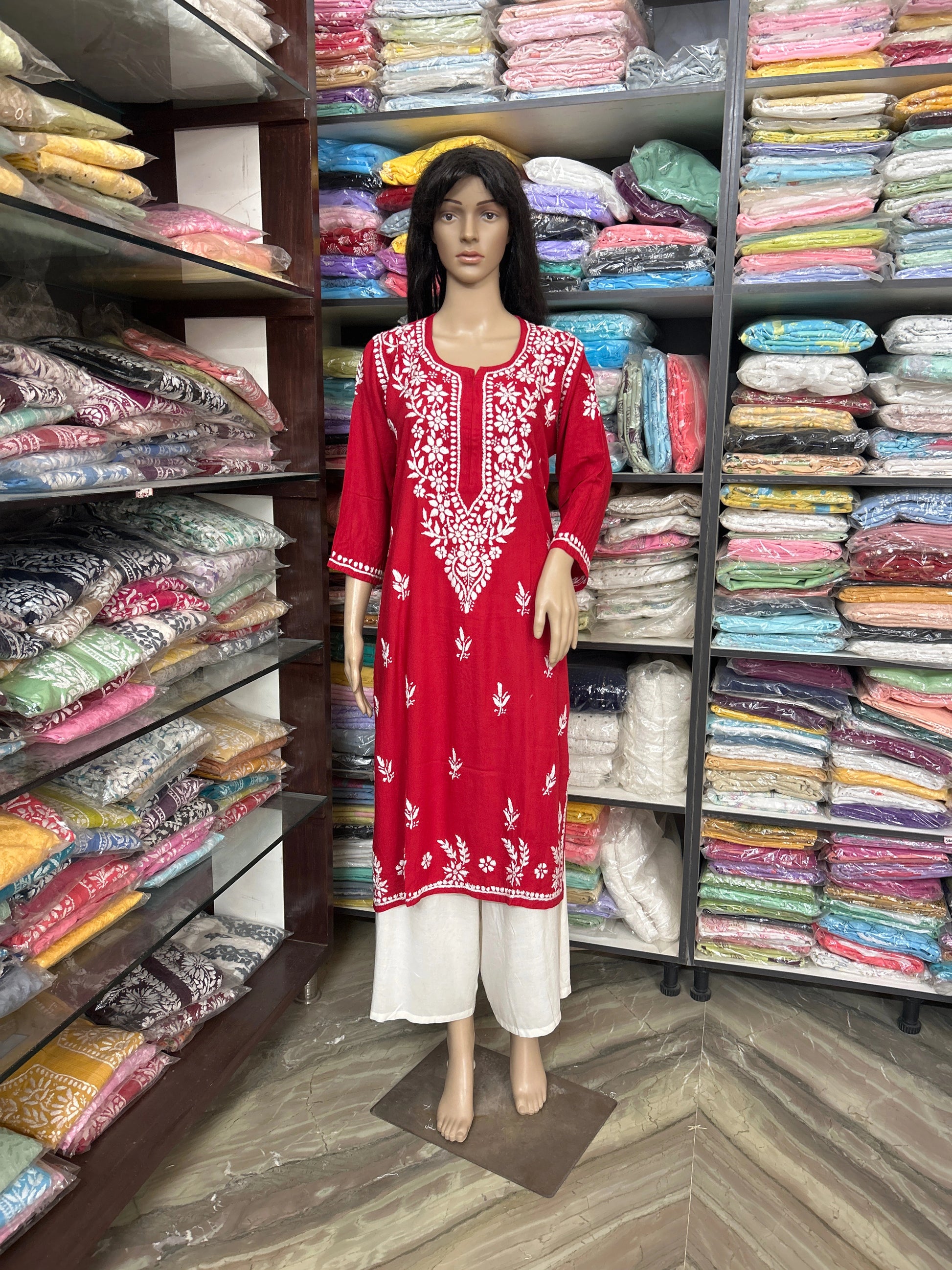 Mannequin wearing a red embroidered dress in a fabric store with shelves of colorful fabrics.