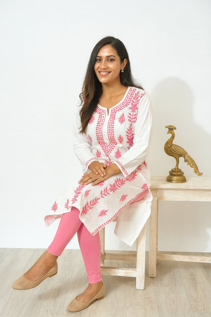 Woman wearing a white and pink embroidered kurta with pink leggings, sitting on a chair.