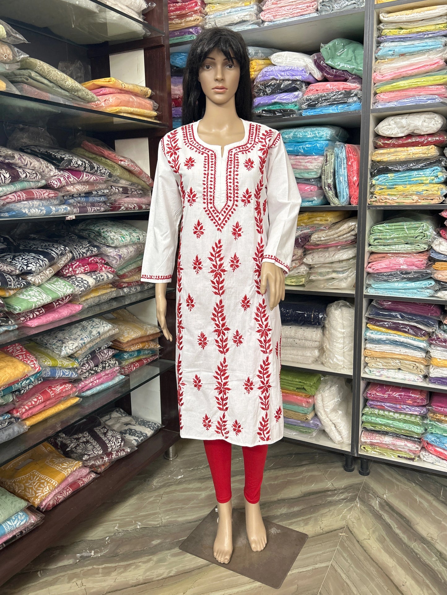 Mannequin wearing a white embroidered dress with red patterns in a fabric store.