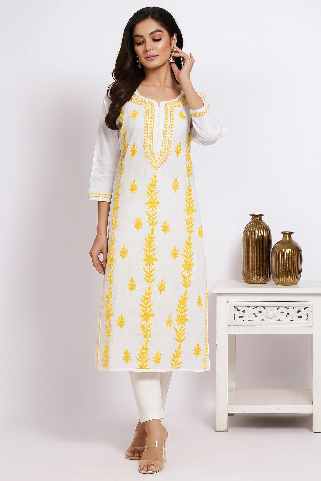 Woman wearing a white kurta with yellow embroidery in a minimalistic setting.