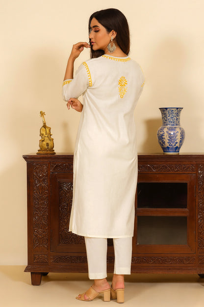 Woman in a white kurta with yellow embroidery standing in front of a wooden cabinet.