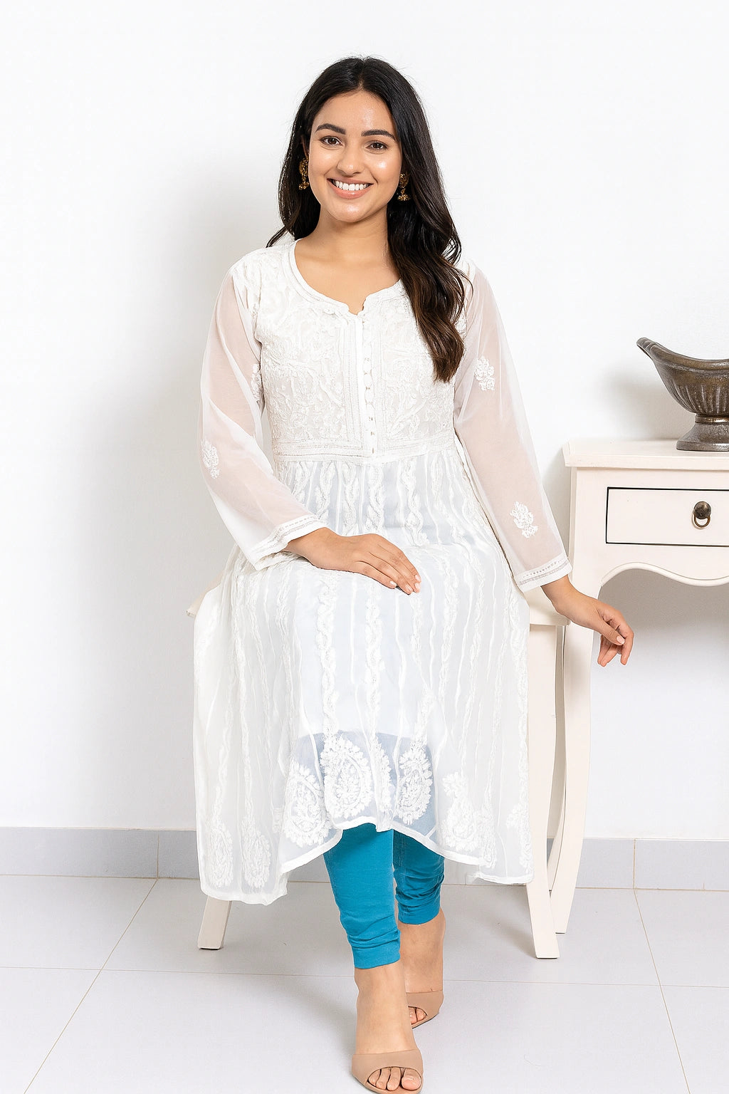 lucknowi chikankari Woman wearing a white kurta with blue pants sitting on a white chair against a white background