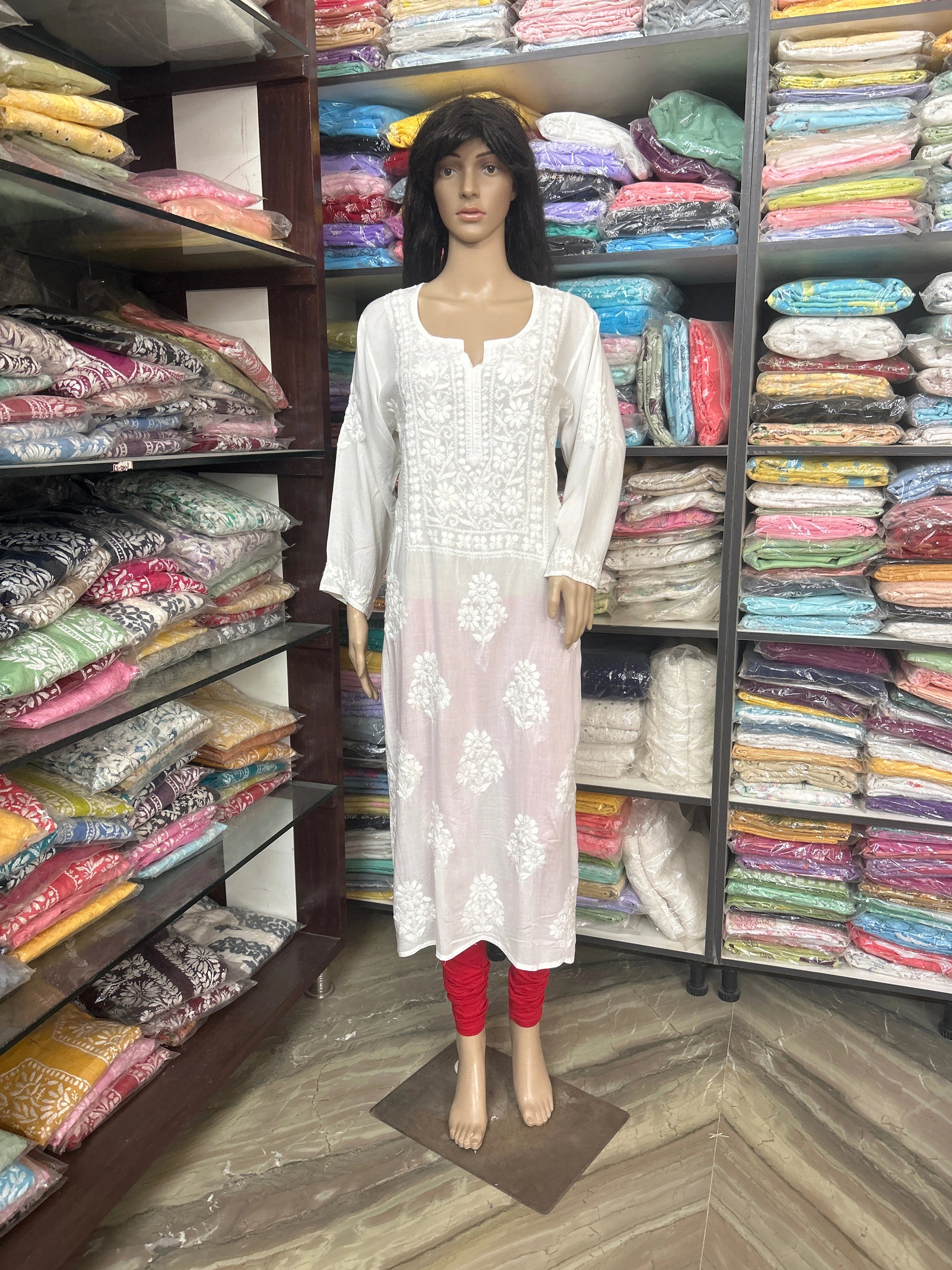 Mannequin wearing a white embroidered kurta with red pants in a fabric store.