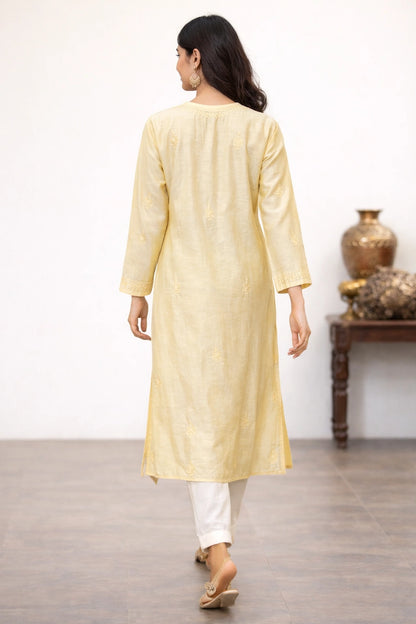 lucknowi chikankari Woman wearing a light yellow kurta with white pants in a room with a wooden table and decorative items.