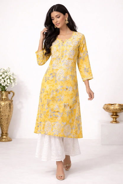 Woman wearing a lucknowi chikankari yellow floral kurta with white pants against a white background