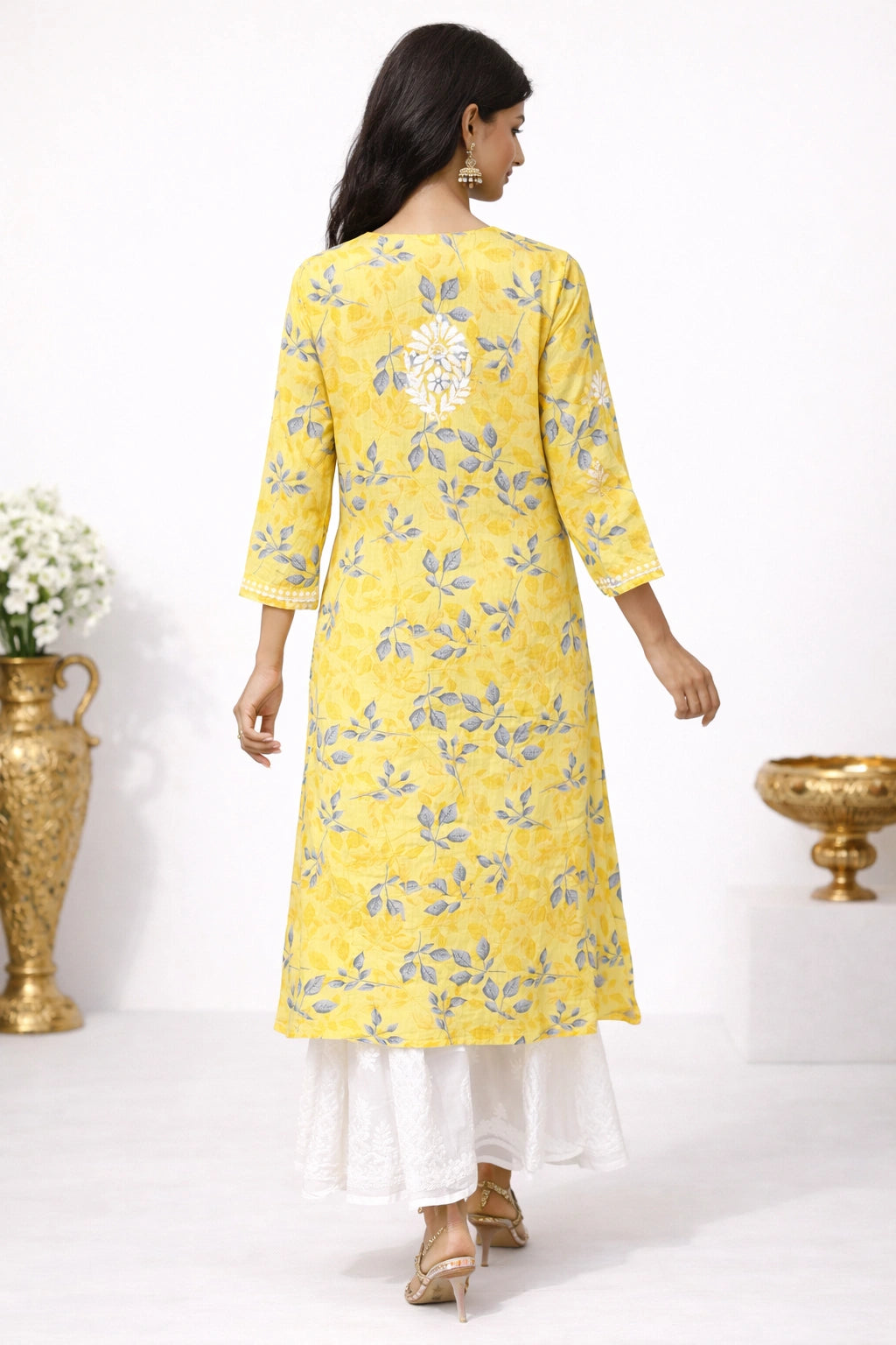 Woman wearing a lucknowi chikankari yellow floral kurta with white pants against a white background