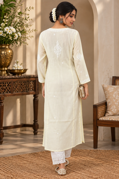 A woman stands in a decorated indoor setting wearing a cream-colored embroidered kurta with matching white pants. The image shows her from the back, highlighting the embroidery on the back of the kurta.
