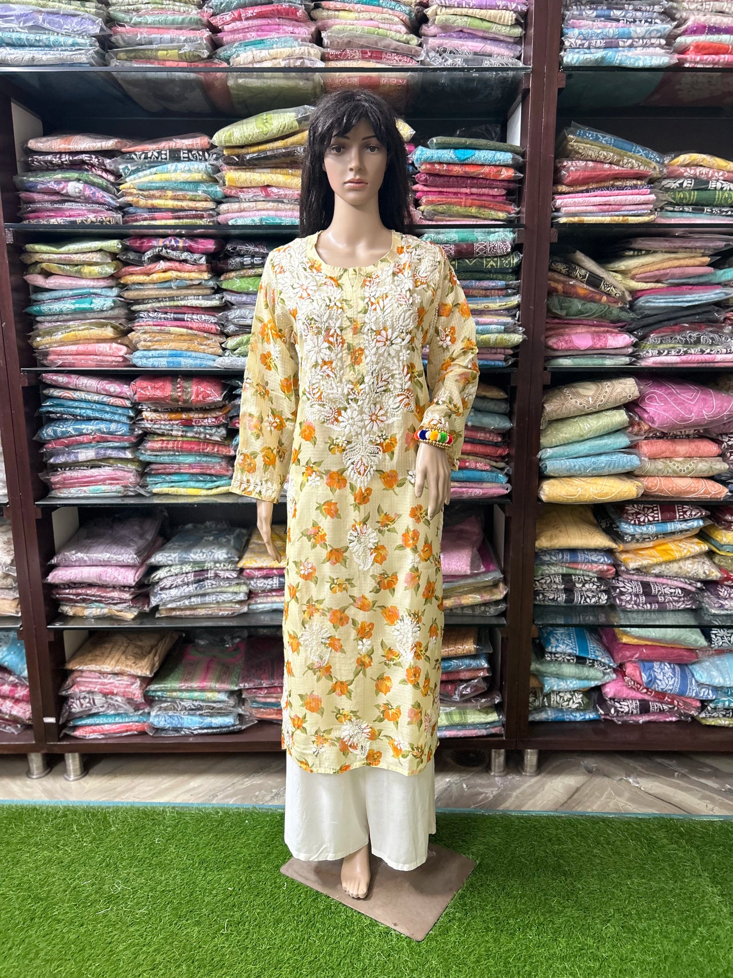 lucknowi chikankari Mannequin wearing a floral dress in front of shelves filled with colorful fabrics.