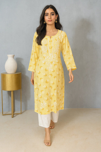 lucknowi chikankari Woman wearing a yellow floral kurta with white pants in a minimalistic setting.