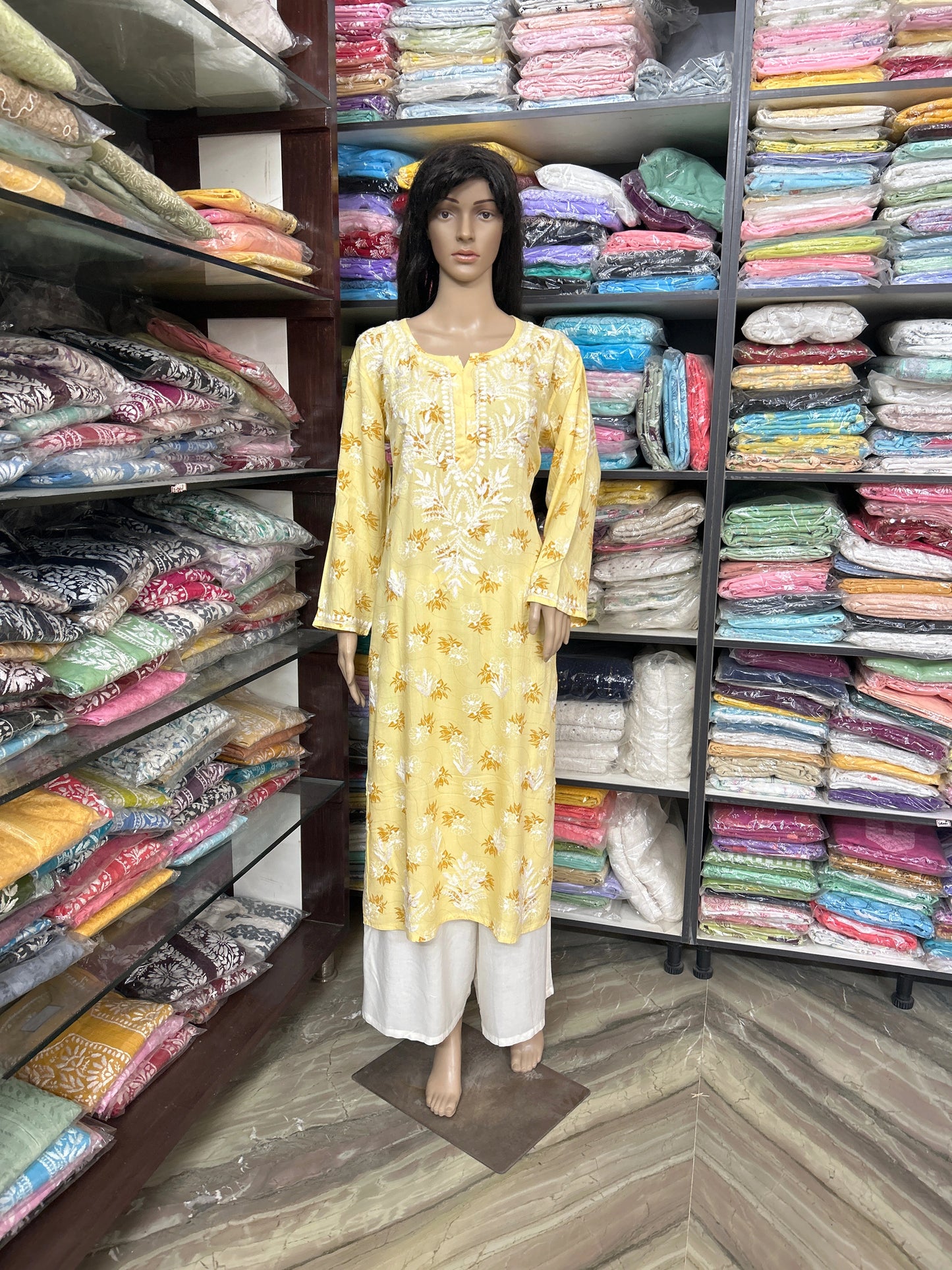 lucknowi chikankari Mannequin wearing a yellow patterned kurta with white pants in a fabric store.