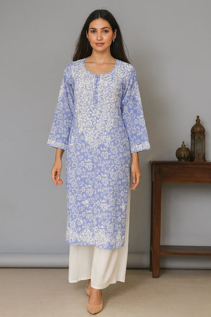 Lucknowi Chikankari Woman wearing a blue floral kurta with white pants in a minimalistic setting.