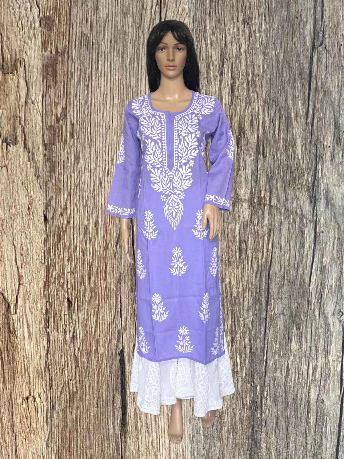 A purple long kurta dress with white floral embroidery and a white lace hem, displayed on a mannequin against a rustic wood plank background.