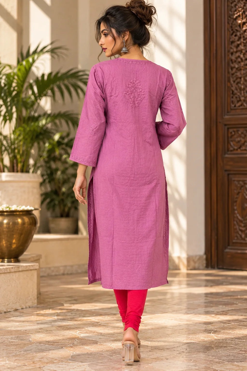 A woman wearing a magenta-pink cotton kurta with three-quarter sleeves and a subtle embroidered motif on the back, paired with bright pink leggings, shown from behind in a sunlit indoor courtyard.