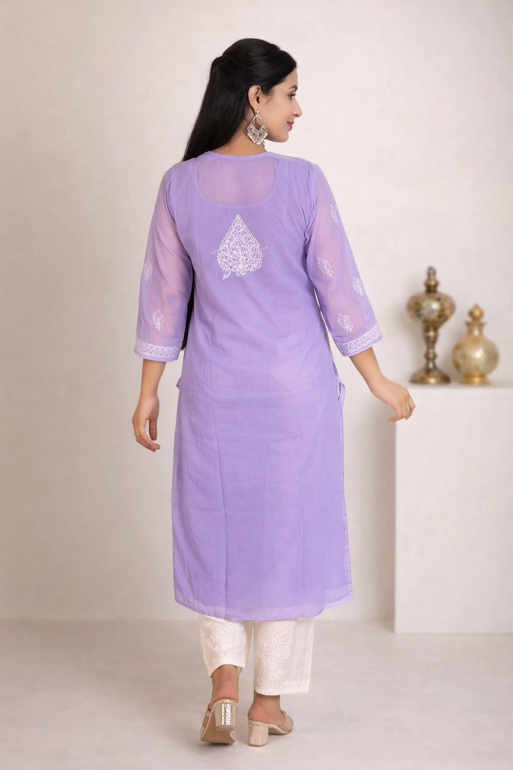 A woman wearing a lavender purple kurta with white embroidery on the back and white pants, shown from the back in a studio setting.