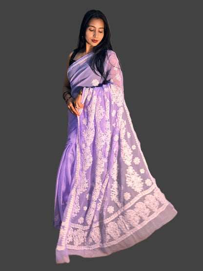 A woman modeling a lavender purple saree with intricate white floral embroidery, set against a solid dark gray background.