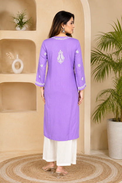 Woman wearing a purple embroidered kurta with white pants in a decorated room.